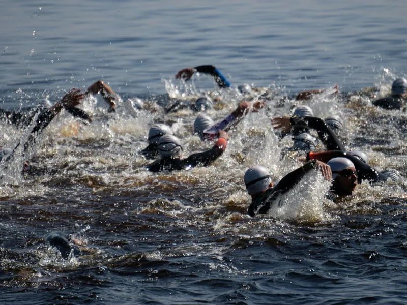 Open-water swimmers in wetsuits and white caps racing through choppy water