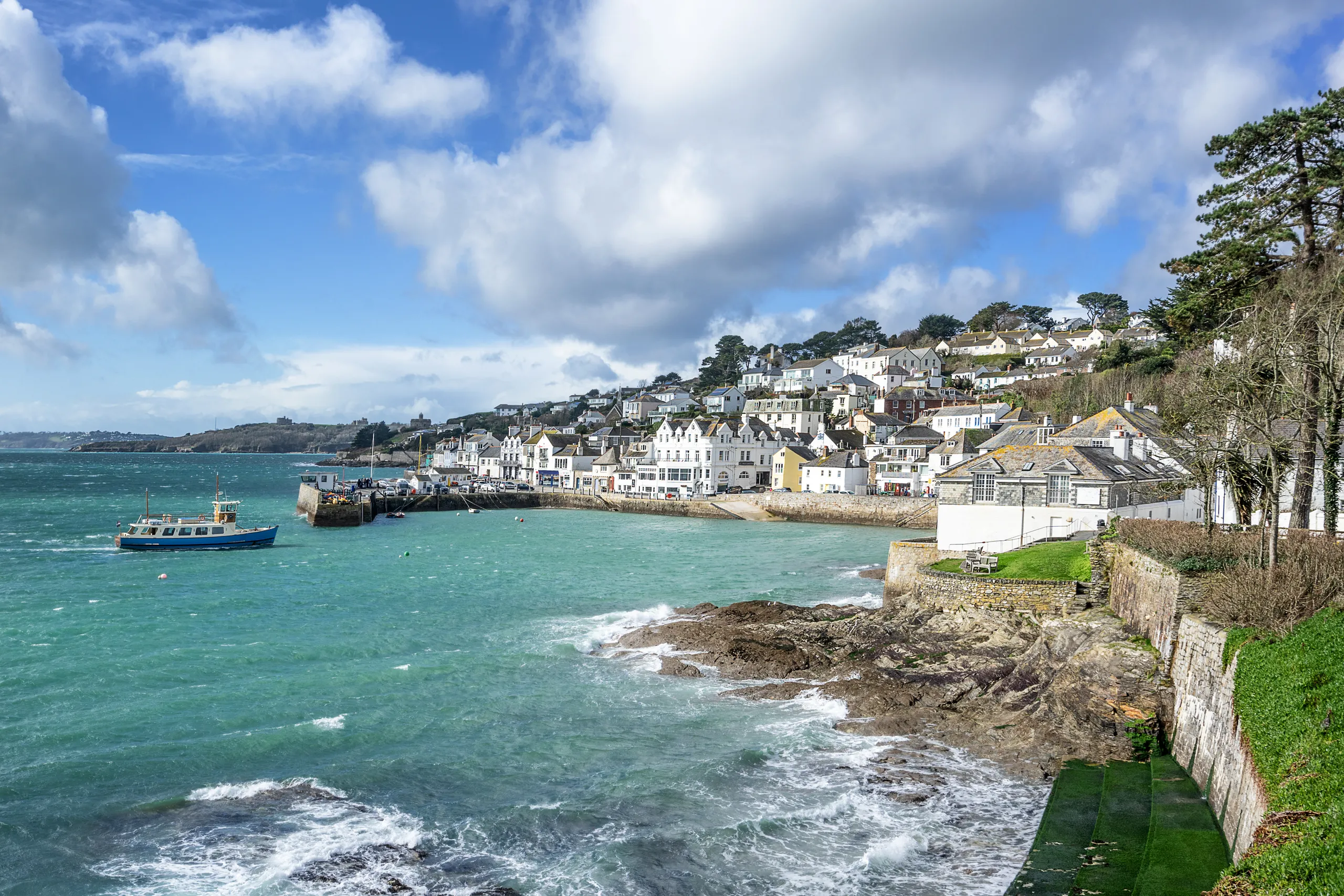 Coastal harbour town with white houses on a hillside, turquoise sea and a small boat under dramatic clouds