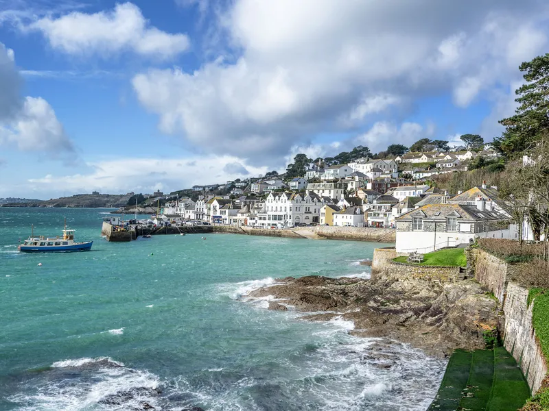 Coastal harbour town with white houses on a hillside, turquoise sea and a small boat under dramatic clouds