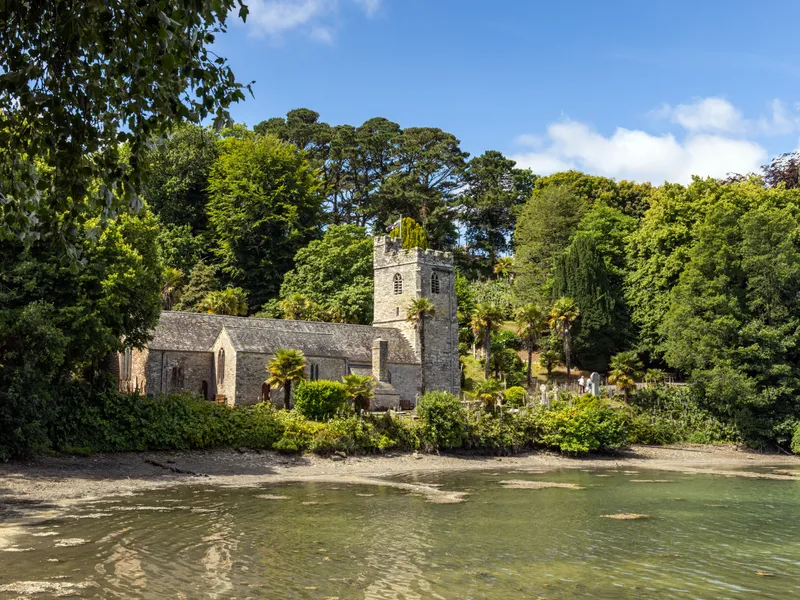 Stone church by a sheltered waterfront surrounded by dense green trees under a blue sky