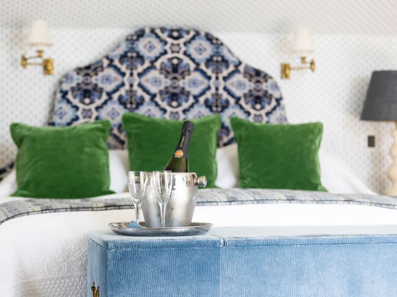 Elegant bedroom with a patterned blue and white headboard, green cushions, and a bottle of champagne in an ice bucket at the foot of the bed