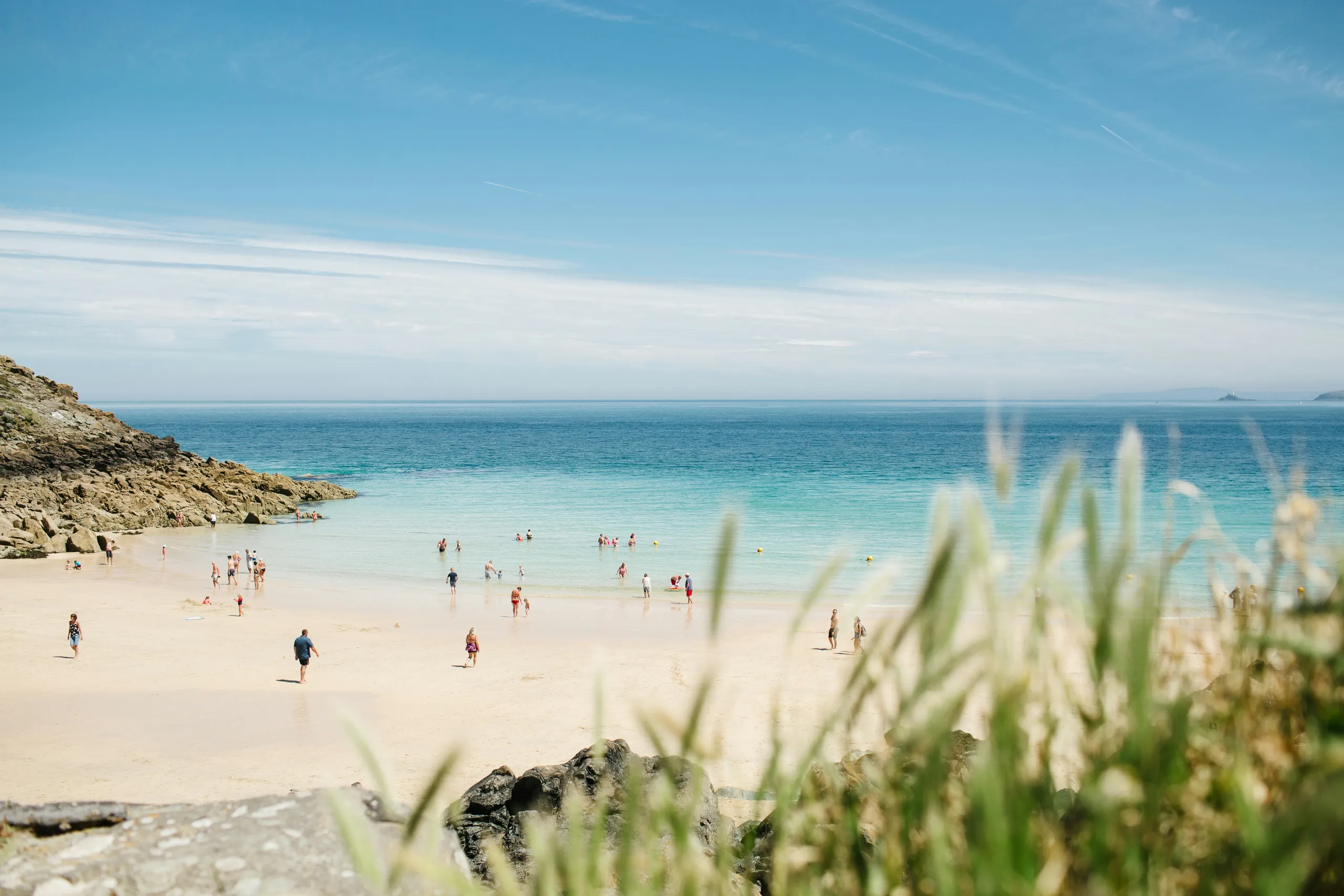 People enjoying a sandy beach with clear turquoise sea and rocky cliffs under a bright blue sky