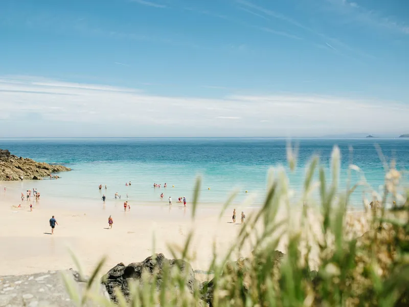 People enjoying a sandy beach with clear turquoise sea and rocky cliffs under a bright blue sky