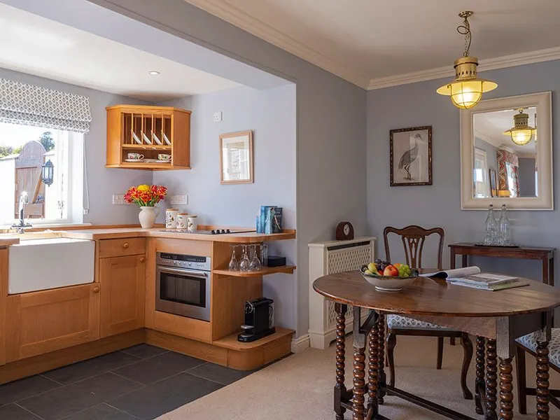Bright kitchen and dining area with wooden cabinets, farmhouse sink, round table and classic chairs