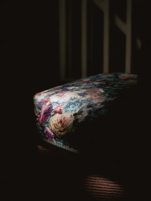 Floral upholstered stool in soft light against a dark interior