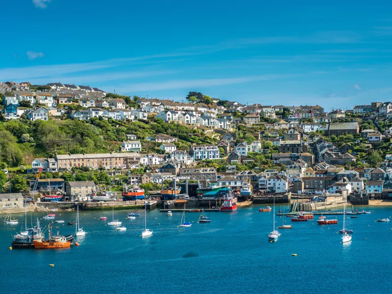 Fowey Hillside coastal village with white and stone houses overlooking a harbour filled with fishing boats and yachts on a bright sunny day