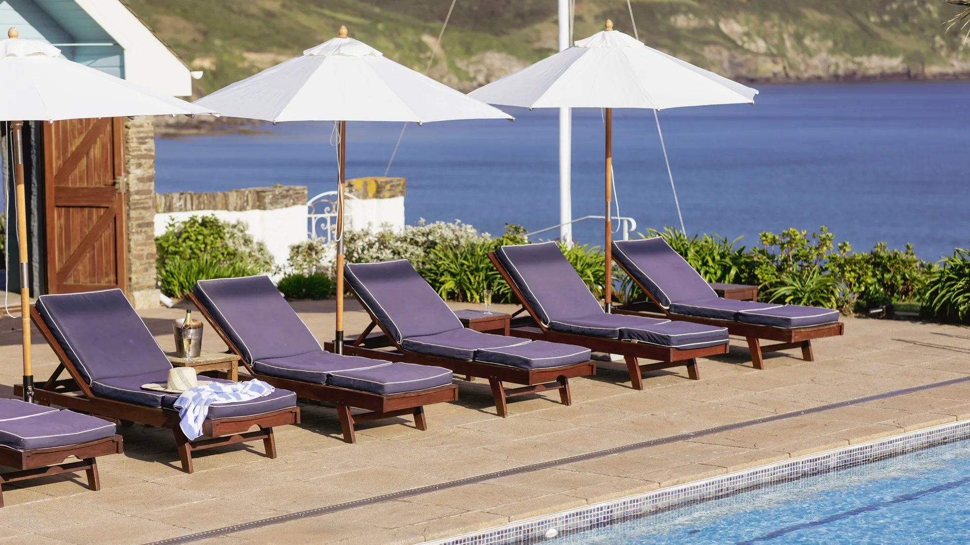 Sun loungers and white parasols beside an outdoor pool overlooking the sea and coastal cliffs