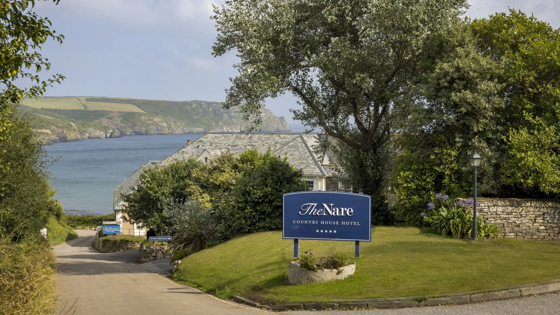 Entrance sign for The Nare Country House Hotel beside a coastal road with sea views and trees