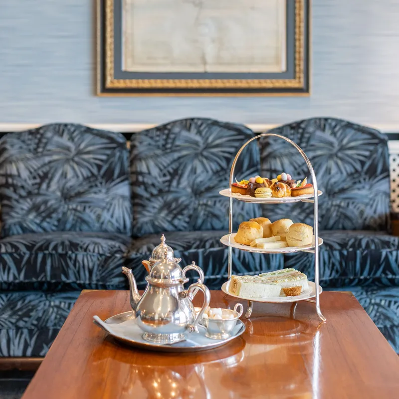 Afternoon tea set on a polished wooden table in front of a patterned sofa and framed wall art