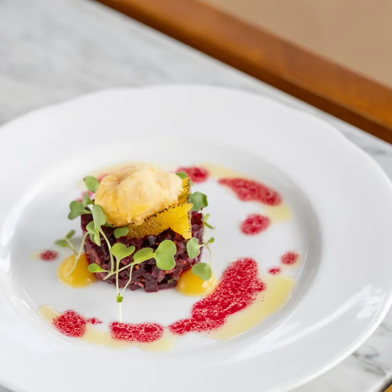 Elegant plated beetroot tartare topped with citrus segments, microgreens and a quenelle on a white plate
