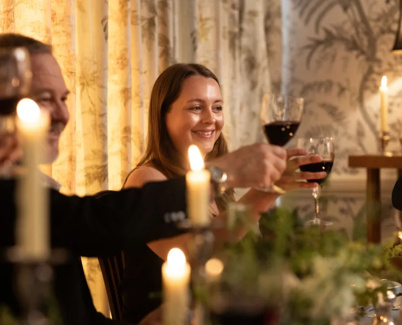 Guests raise glasses of red wine in a candlelit dining room during a cosy dinner party.