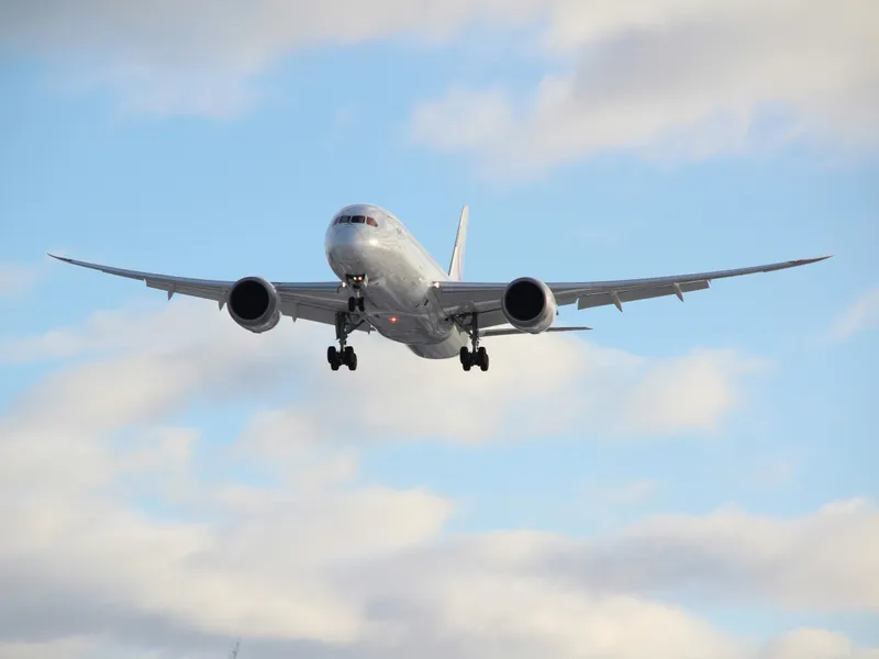 Front view of a commercial aeroplane descending with landing gear down against a blue sky with clouds