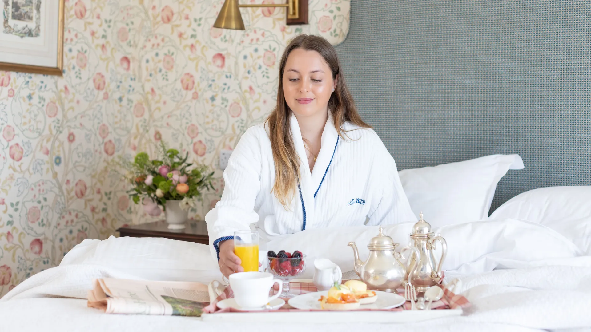 Woman in a white dressing gown enjoying breakfast in bed in an elegant floral bedroom