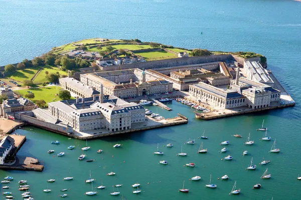 Aerial view of The Nare at Mayflower marina in Plymouth, showing historic stone buildings, harbour walls and moored sailing boats on blue water.