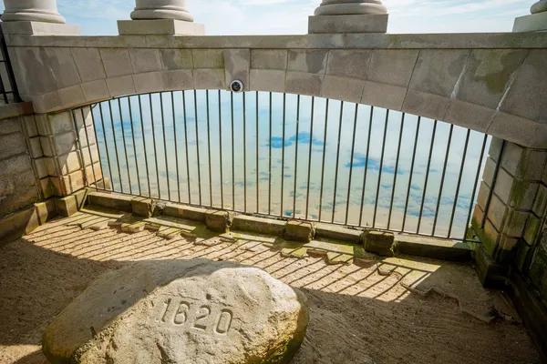Stone marked 1620 beneath tall columns at a coastal viewpoint overlooking the sea under a bright blue sky.