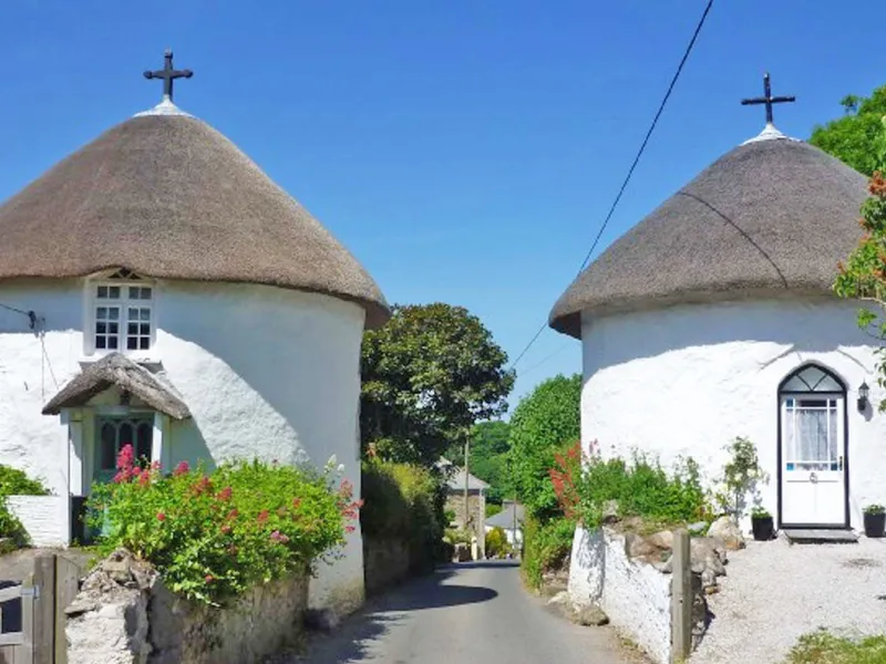 Two whitewashed round houses with thatched roofs beside a narrow lane in Veryan, Cornwall