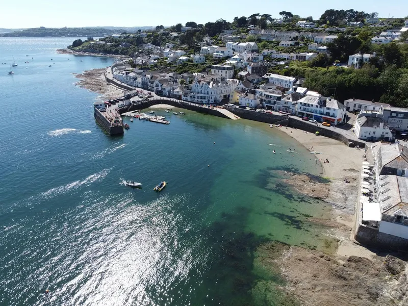 Aerial view of the picturesque coastal village St Mawes with a small harbour, sandy beach and clear turquoise sea on a sunny day.
