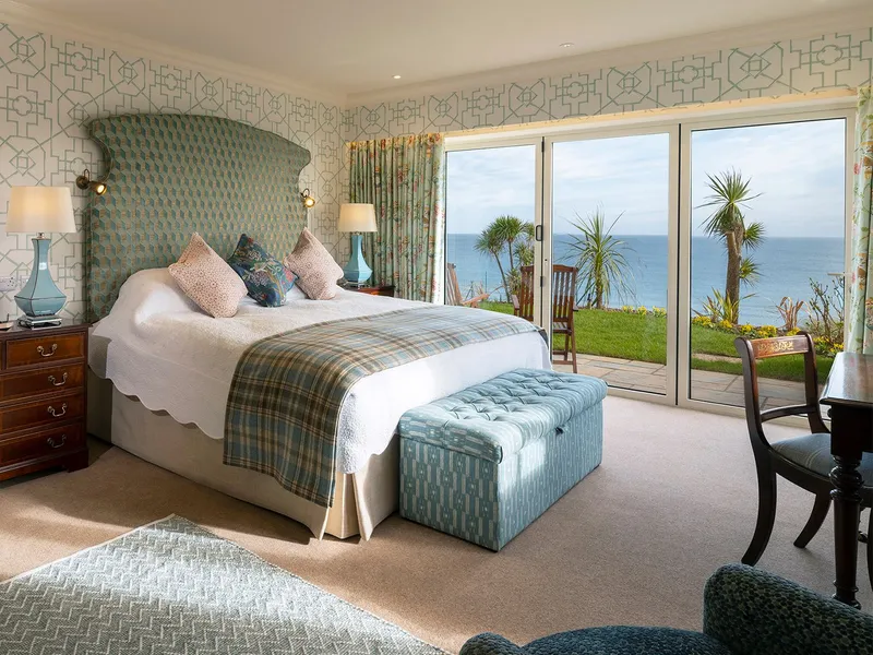 Elegant seaside bedroom suite with patterned wallpaper, a large upholstered bed, and sliding doors opening to an ocean view terrace.