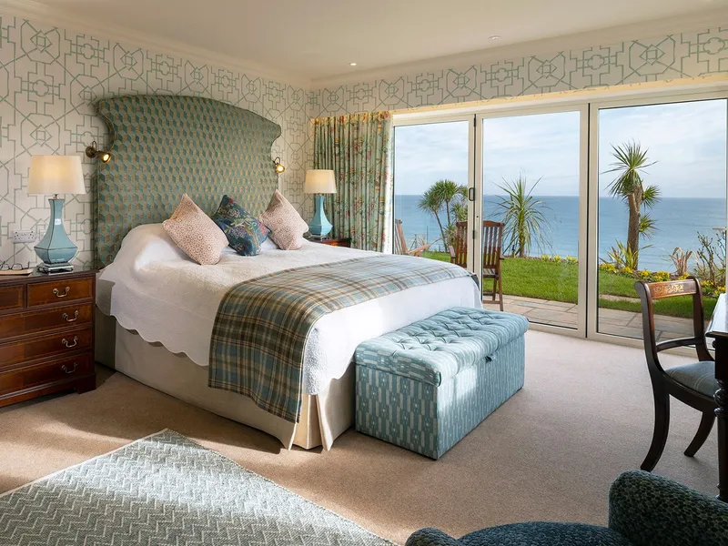 Elegant seaside bedroom suite with patterned wallpaper, a large upholstered bed, and sliding doors opening to an ocean view terrace.
