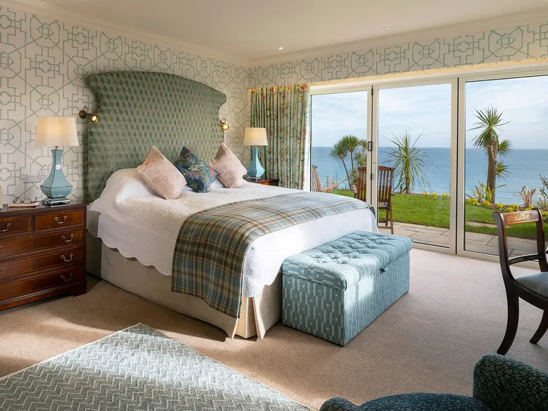 Elegant seaside bedroom suite with patterned wallpaper, a large upholstered bed, and sliding doors opening to an ocean view terrace.