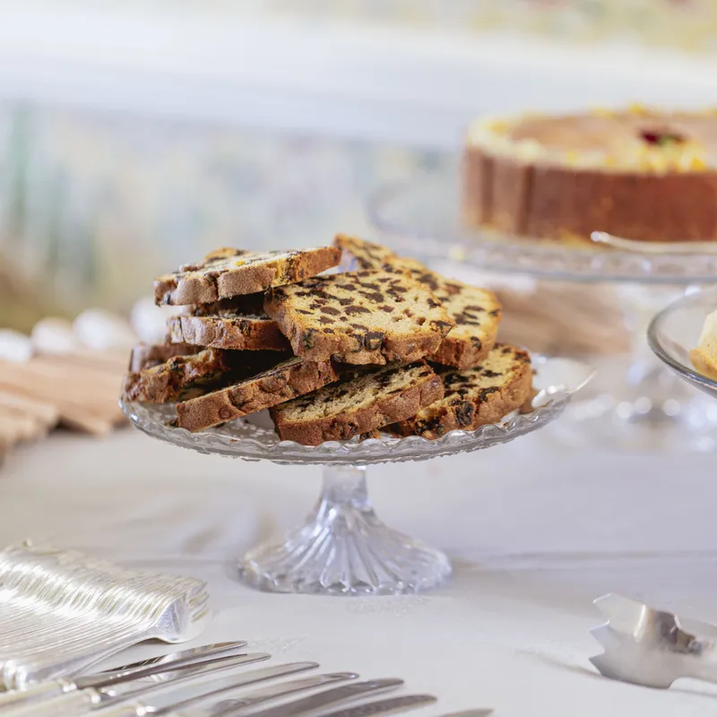 Slices of fruit loaf arranged on a glass cake stand at a dessert table with silver cutlery in the foreground