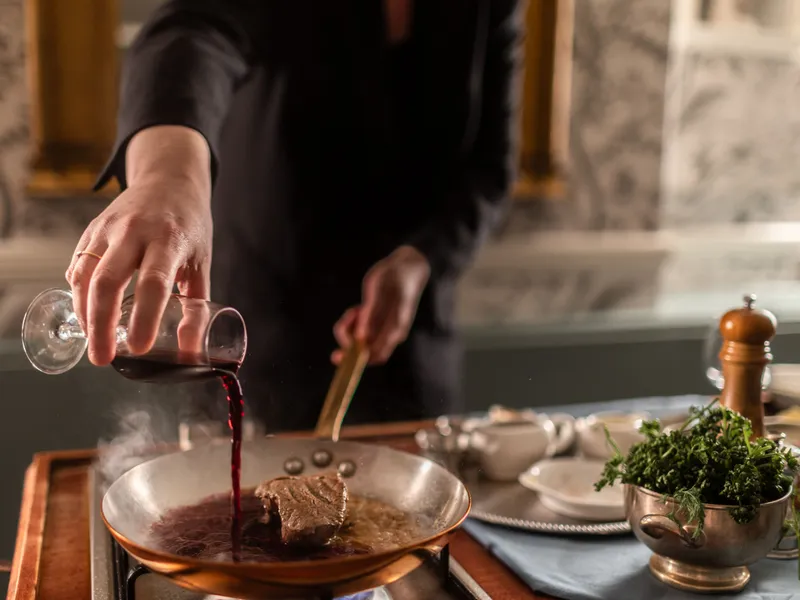 Chef pouring red wine into a pan with a steak cooking on the hob
