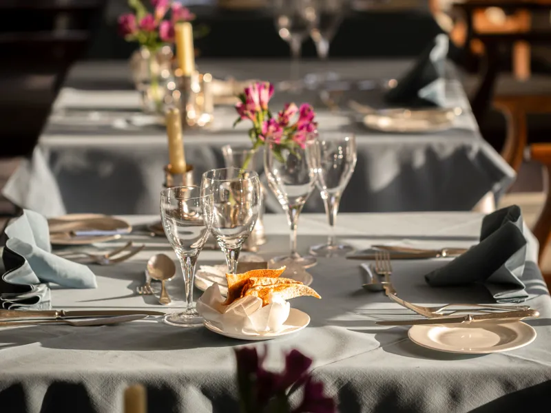 Elegantly set restaurant tables with candles, glassware and small pink floral arrangements in warm natural light