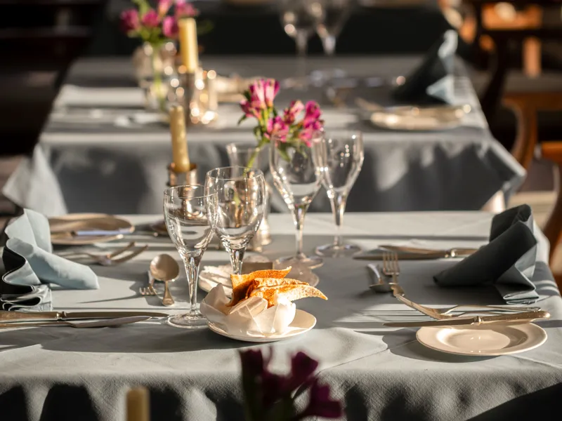 Elegantly set restaurant tables with candles, glassware and small pink floral arrangements in warm natural light