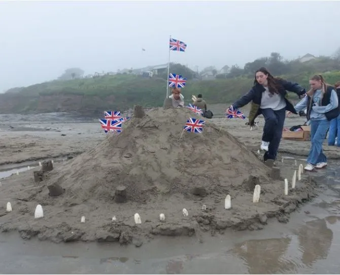 Children decorating a large sandcastle with Union Jack flags on a misty beach
