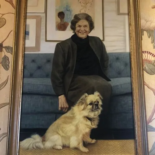 Framed portrait of an elderly woman seated on a blue sofa with a small cream-coloured dog in the foreground