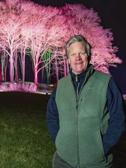 Man standing in front of trees illuminated with pink lights at night