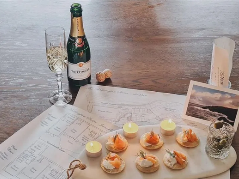 Bottle of Champagne, glass, floor plans and smoked salmon canapés arranged on a wooden table