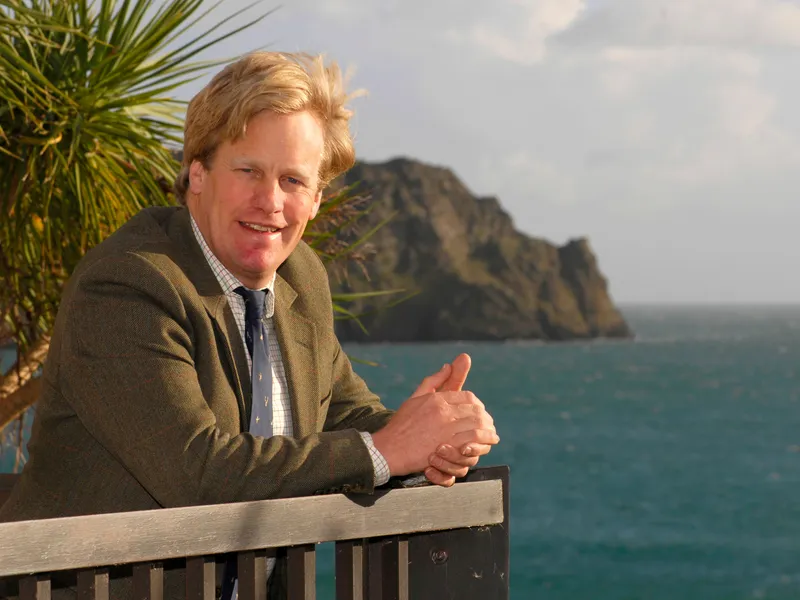 Toby Ashworth leaning on a railing beside the sea with a rocky headland in the background