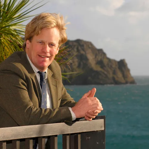 Toby Ashworth leaning on a railing beside the sea with a rocky headland in the background