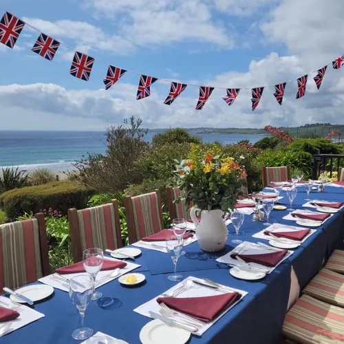 Outdoor dining table set beside the sea with Union Jack bunting overhead and flowers in the centre