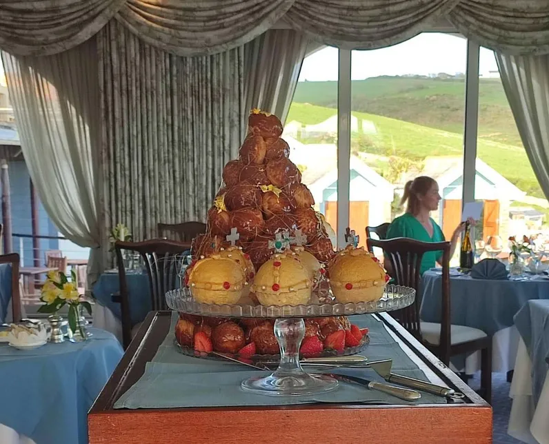 Dessert trolley in a restaurant dining room with profiteroles, cream pastries, strawberries and raspberry puddings by large windows overlooking green hills.