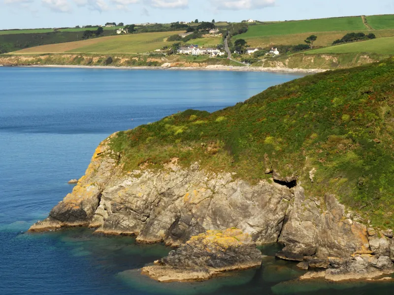 Rocky coastal headland with green cliffs overlooking calm blue sea and patchwork fields in the distance
