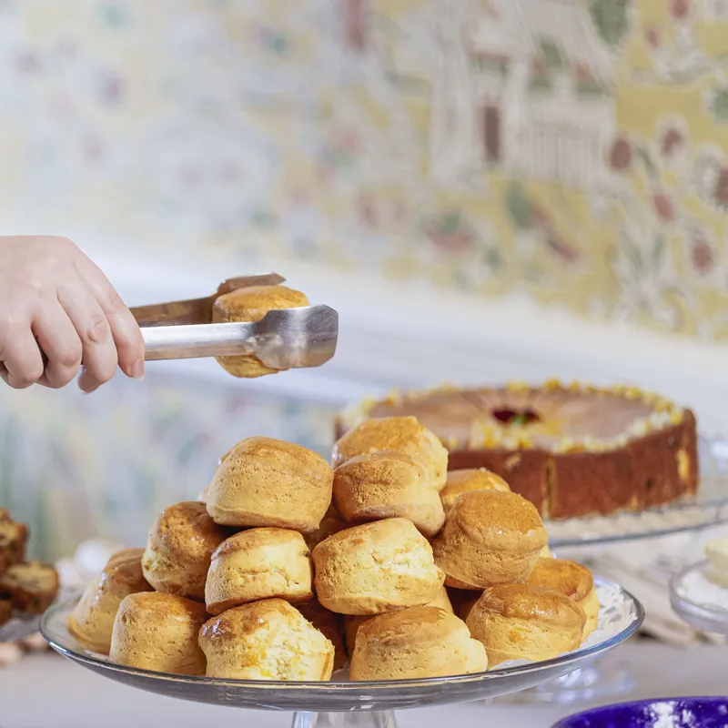 Person using tongs to serve scones from a cake stand at an afternoon tea buffet