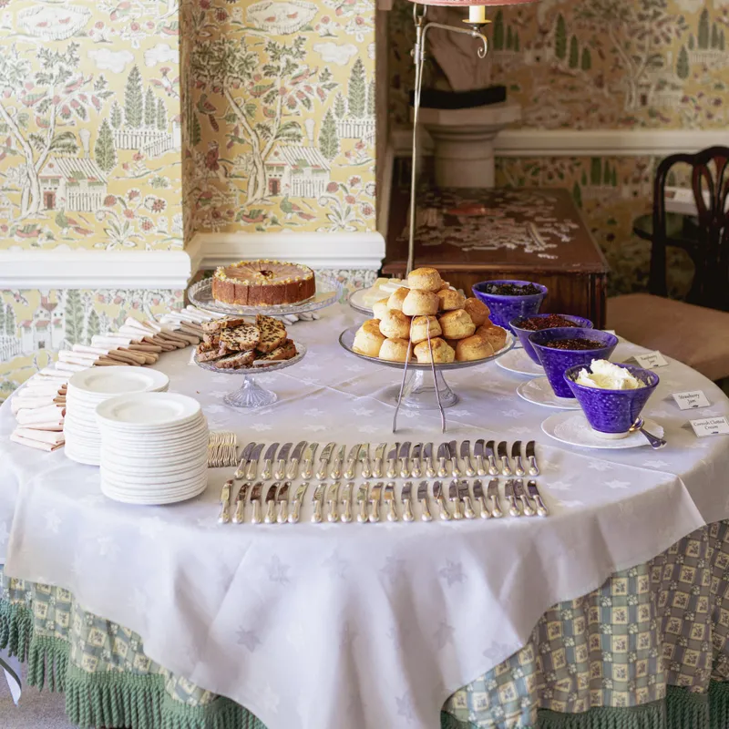 Afternoon tea table with scones, cakes and preserves set against patterned yellow wallpaper in a traditional interior