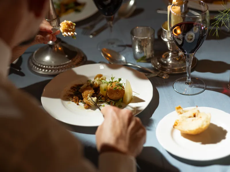 Person dining at an elegant candlelit table with a plated gourmet dish and a glass of red wine
