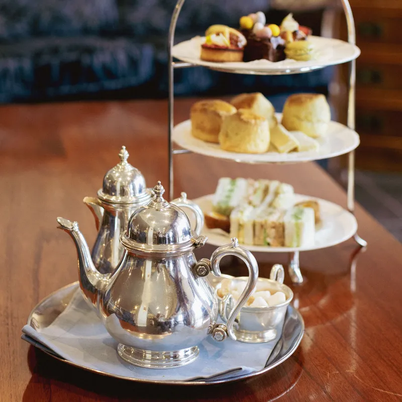 Traditional afternoon tea with silver teapots, finger sandwiches, scones and pastries on a tiered stand