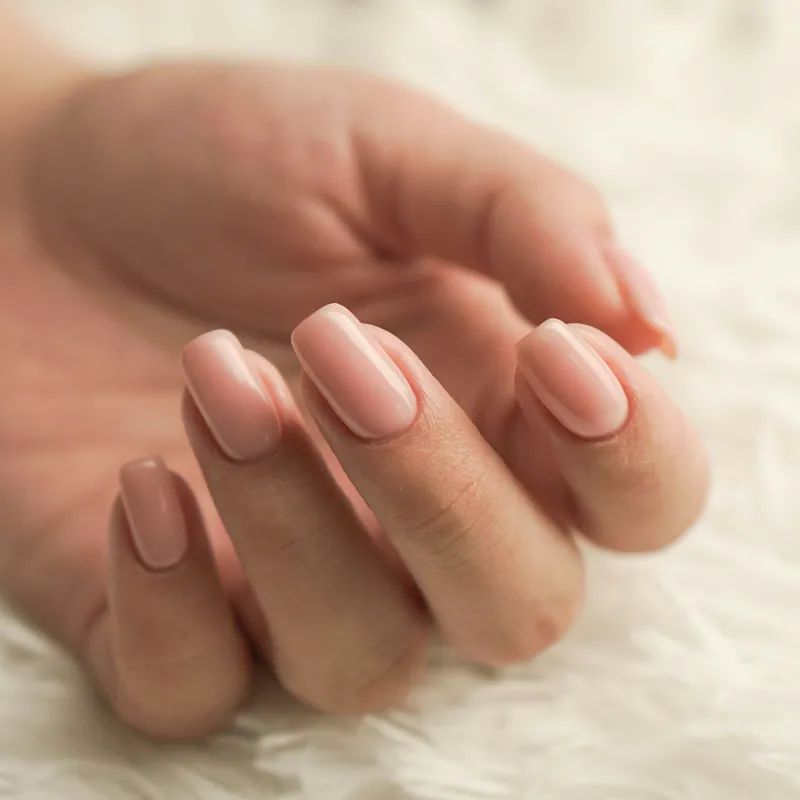 Close-up of a hand with pale pink manicured nails resting on a soft white surface.