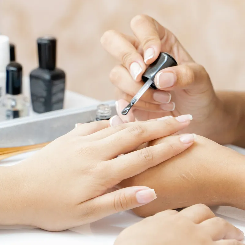 Close-up of a beautician applying clear nail polish during a manicure.