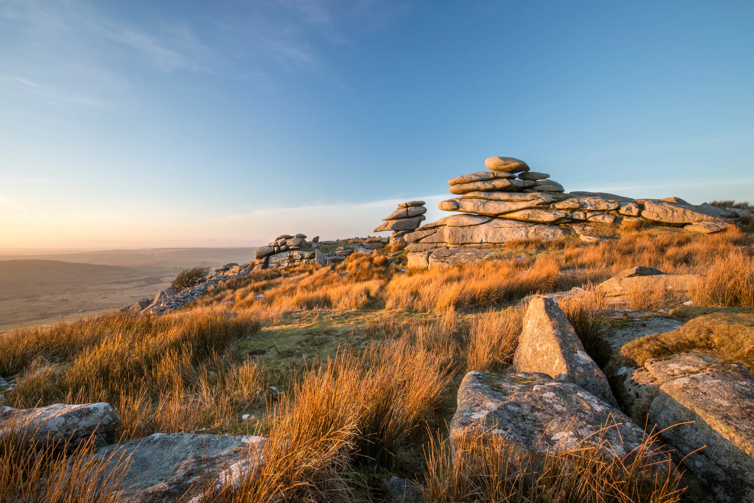 Rocky moorland landscape at sunrise with granite tors and golden grass under a clear blue sky