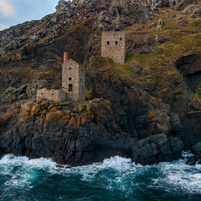 Stone engine houses on a rugged cliff above crashing sea waves