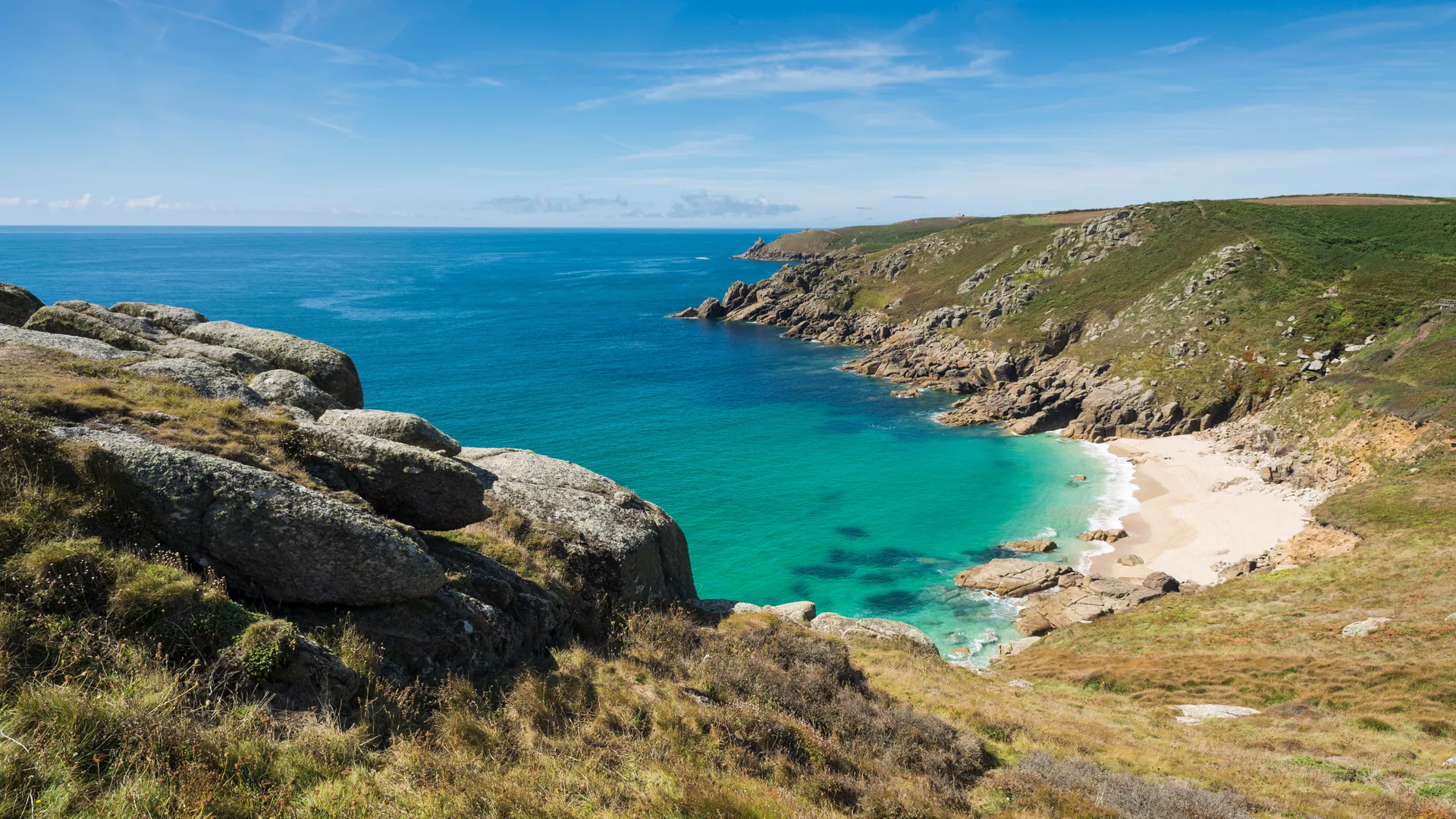 Porth Chapel Beach on Penwith Peninsula Rocky coastal cove with turquoise sea, white sandy beach and grassy cliffs under a blue sky