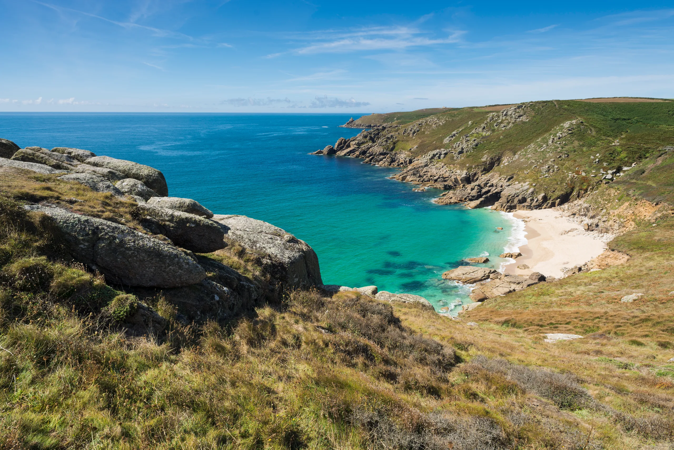 Porth Chapel Beach on Penwith Peninsula Rocky coastal cove with turquoise sea, white sandy beach and grassy cliffs under a blue sky