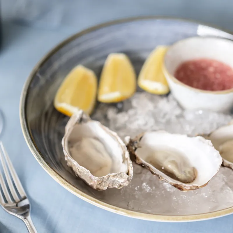 Fresh oysters served on crushed ice with lemon wedges and a small dish of red sauce