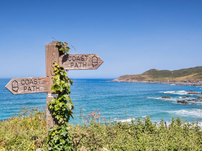 South West Coast Path Wooden coast path signpost beside a turquoise sea and rocky headland under a clear blue sky