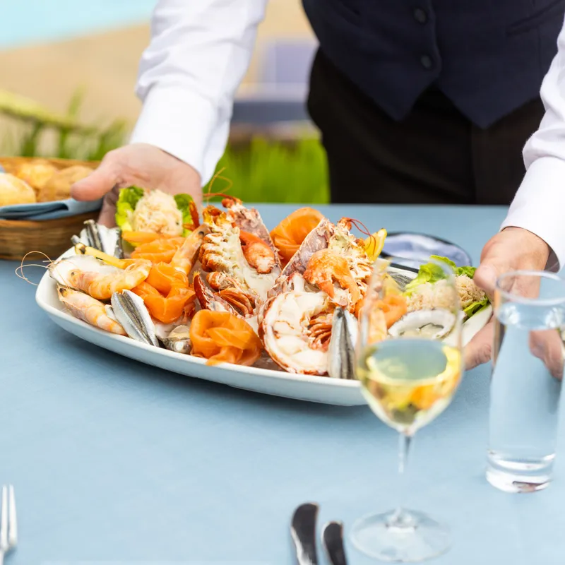 Server placing a seafood platter with lobster, prawns and salmon on a restaurant table